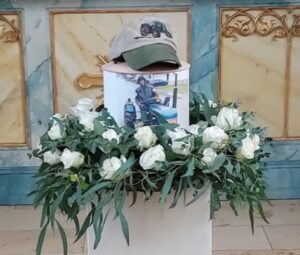 Urne bei der Trauerfeier. Fotourne auf sockel mit Rosen und einem Basecap auf der Urne